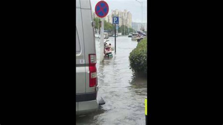 Two people walking through floodwaters next to homes